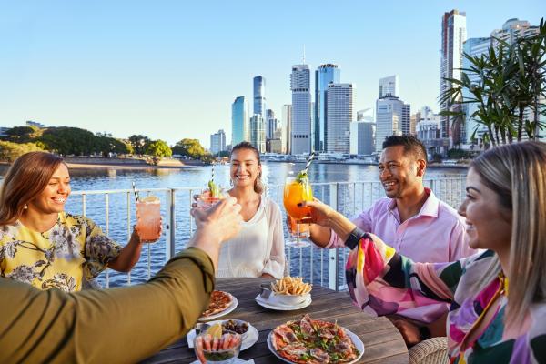 A group of friends alfresco dining and cheering over cocktails at riverside Brisbane